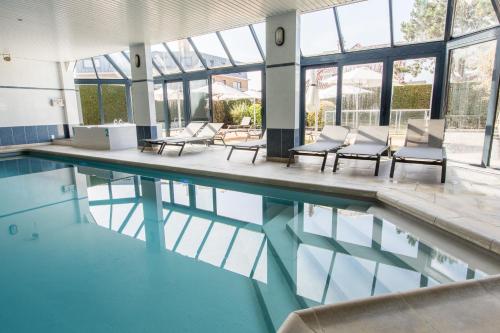 a swimming pool with chairs and tables and windows at Hotel Apostroff in Koksijde