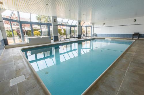 a large swimming pool with blue water in a building at Hotel Apostroff in Koksijde