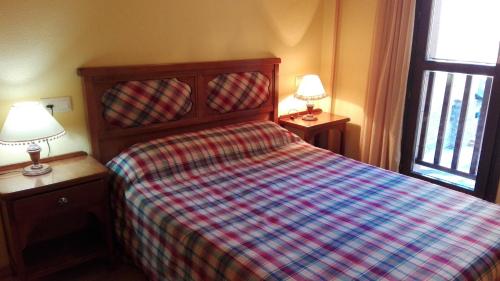 a bedroom with a bed with a plaid blanket and two lamps at Apartamentos Ball Benas Edificio Prados de Velarta in Cerler