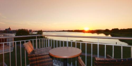 a table and chairs on a balcony with the sunset at Hotel Warnow in Rostock