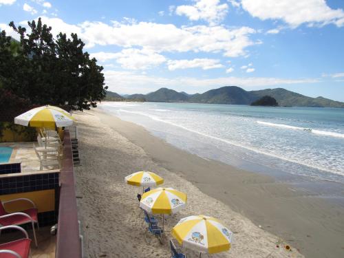 a beach with yellow and white umbrellas and the ocean at Pousada Casa na Praia in Ubatuba
