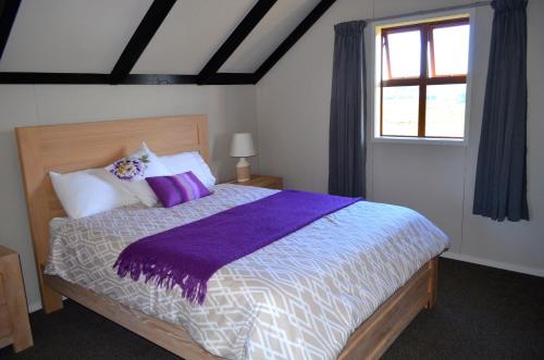 a bedroom with a bed with purple sheets and a window at A Touch of Tuscany at Hillsborough in New Plymouth