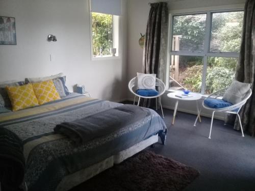 a bedroom with a bed and two chairs and a window at Harbour Lights Hideaway in Whitianga