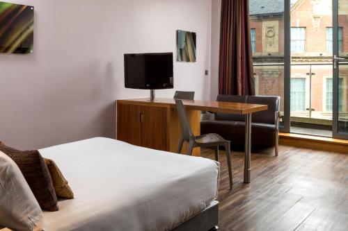 a hotel room with a bed, desk and television at Roomzzz Leeds City in Leeds