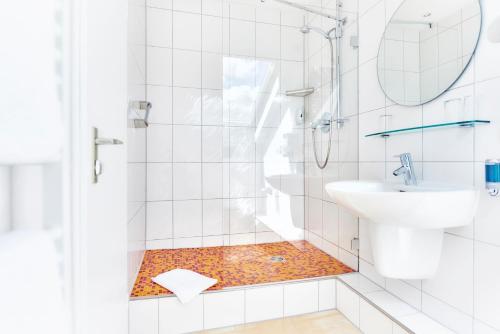 a white bathroom with a shower and a sink at Waldhotel Sulzbachtal in Schönaich