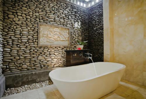 a bath tub in a bathroom with a stone wall at Sri Ratih Cottages, CHSE Certified in Ubud