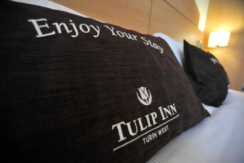 a black pillow on a bed with the words enjoy your stay at Tulip Inn Turin West Rivoli in Rivoli