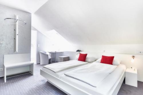 a white bedroom with a large white bed with red pillows at Waldhotel Sulzbachtal in Schönaich