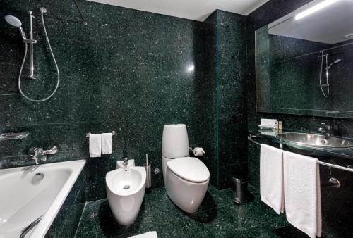 a bathroom with a toilet and a tub and a sink at Neat Hotel Avenida in Ponta Delgada