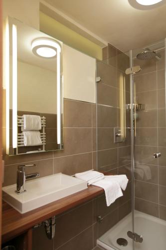a bathroom with a sink and a mirror and a shower at Hotel Peterhof - urban lifestyle Kempten in Kempten
