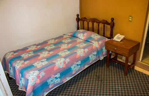 ein Schlafzimmer mit einem Bett und einem Telefon neben einem Tisch in der Unterkunft Hotel María Elena in Lagos de Moreno