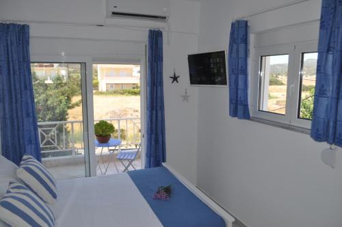 a bedroom with a bed with blue curtains and a balcony at Villa Imerti Kiotari in Kiotari