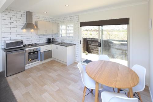 a kitchen with a wooden table and white chairs at Te Whau Bach Apartments in Te Whau Bay
