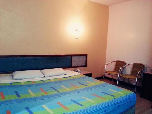 1 Schlafzimmer mit einem Bett mit einer farbenfrohen Tagesdecke und 2 Stühlen in der Unterkunft Monaco Dynasty Hotel in Tawau