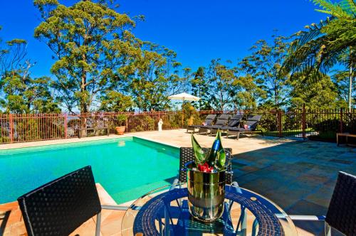 a table with chairs next to a swimming pool at Possum Lodge At Cloudhill Estate in Mount Tamborine