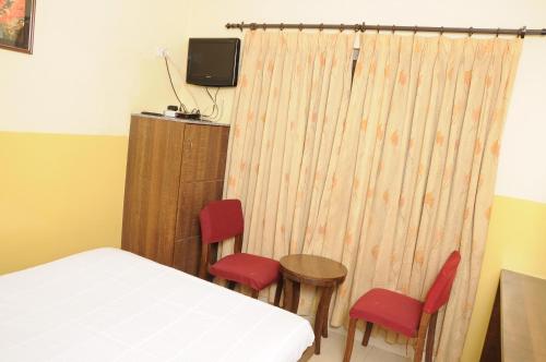a bedroom with a bed and two red chairs at Suvarna Compact in Mysore