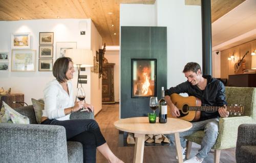 a man playing a guitar while a woman plays a guitar in a living room at Hotel Condor in San Vigilio Di Marebbe