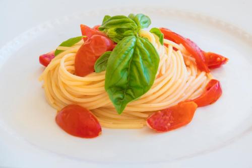 a plate of pasta with tomatoes and basil on it at Hotel Dei Pini in Alghero