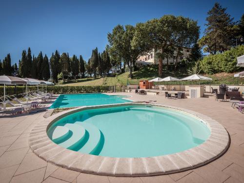 グッビオにあるHotel Villa Montegranelliの大型スイミングプール(椅子、パラソル付)