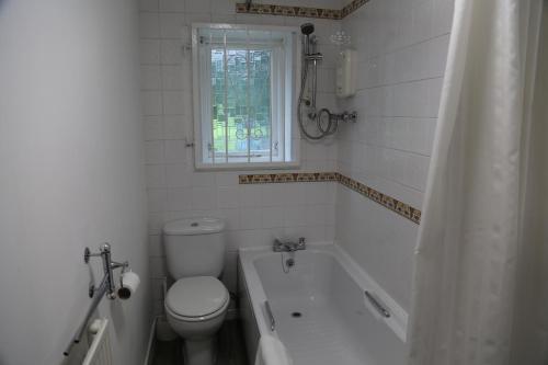 a bathroom with a toilet and a tub and a window at La Suisse Serviced Apartments in Manchester
