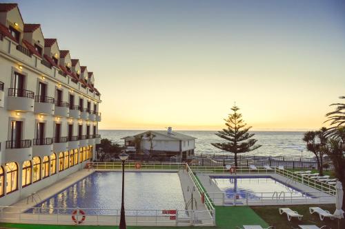a hotel with a swimming pool in front of the ocean at Hotel Restaurante Glasgow in Villadesuso