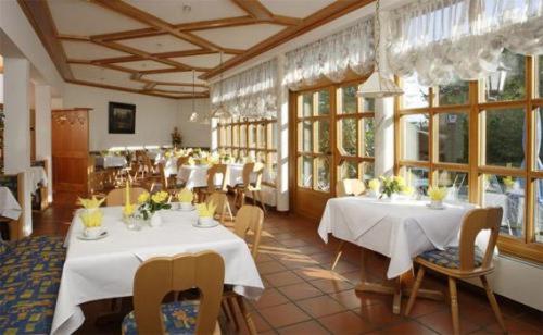 un restaurante con mesas y sillas blancas y ventanas en Hotel Landgasthof Gschwendtner, en Allershausen