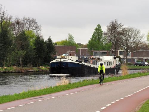 a person riding a bike down a road next to a boat at Hotelboot Sarah in Amsterdam