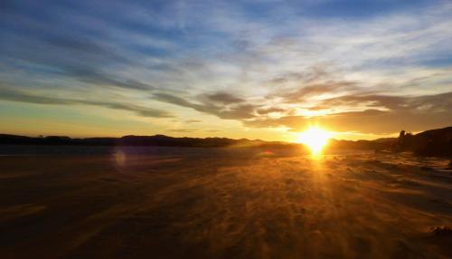 a sunset on a beach with the sun in the sky at Surat Bay Lodge by the Sea/Backpackers Hostel in Owaka