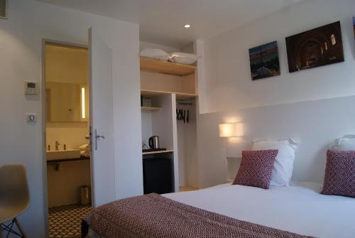 a bedroom with a white bed and a kitchen at Contact Hôtel Le Minervois - Hôtel & Restaurant Au nord de Carcassonne in Caunes-Minervois