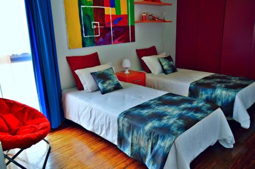 Cette chambre comprend deux lits et un fauteuil rouge. dans l'établissement vista dos arrifes, à Funchal