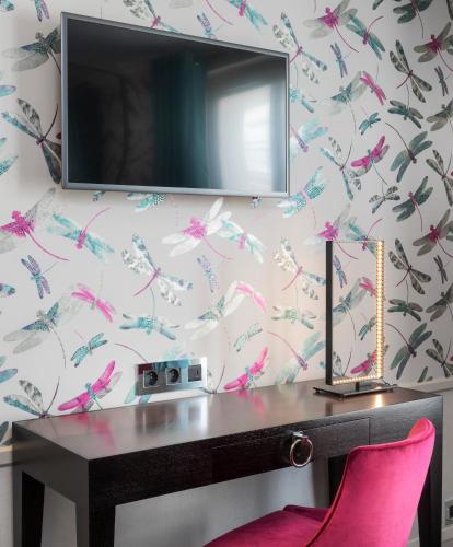 Elle comprend un bureau avec une chaise rose et une télévision murale. dans l'établissement Vendôme Opera Hotel, à Paris