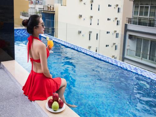 a woman in a red dress sitting next to a swimming pool at Red Sun Nha Trang Hotel in Nha Trang
