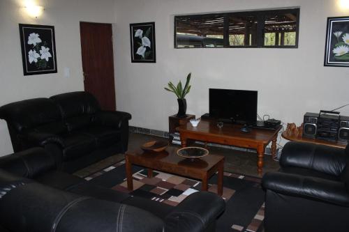 a living room with black leather furniture and a table at Woodpecker Lodge B&B in Hoedspruit