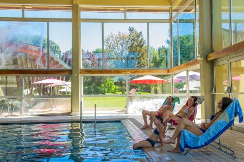 three women sitting in chairs next to a swimming pool at VTF Le Domaine des Puys in Saint-Sauves- dʼAuvergne