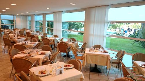 a dining room with tables and chairs and windows at Hotel Mediterraneo in Lignano Sabbiadoro