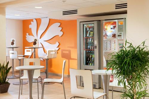 a restaurant with white tables and chairs and an orange wall at Premiere Classe Pau Est-Bizanos in Pau