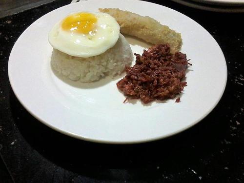 a plate of food with an egg on top of rice at Fj Manila Hotel in Daraga