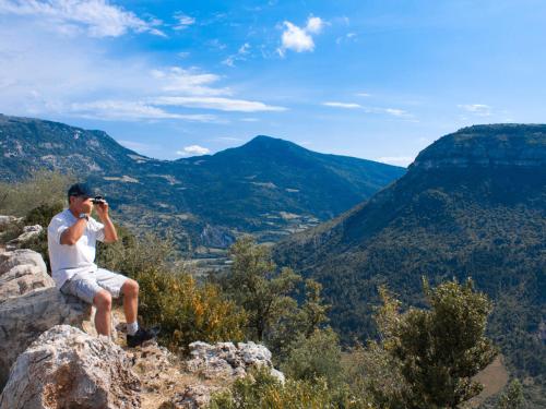 a man sitting on a rock taking a picture of the mountains at Village Club Les Lavandes - Neaclub in Rémuzat