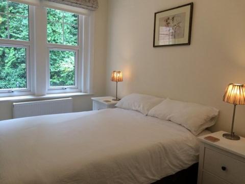 a bedroom with a white bed and two windows at Brockenhurst Apartments in Brockenhurst