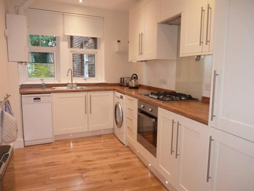 cocina con armarios blancos y suelo de madera en Brockenhurst Apartments, en Brockenhurst