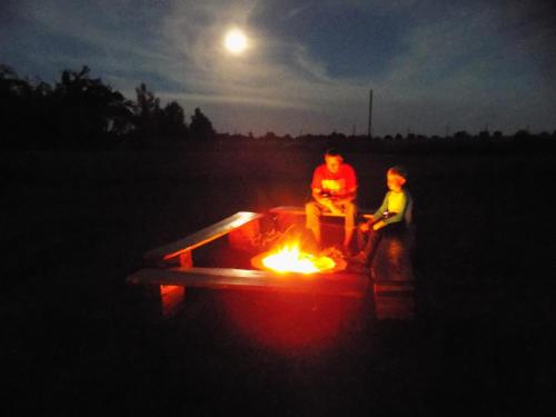 two people sitting around a fire in a field at night at Holiday House Adrelot in Heřmaničky