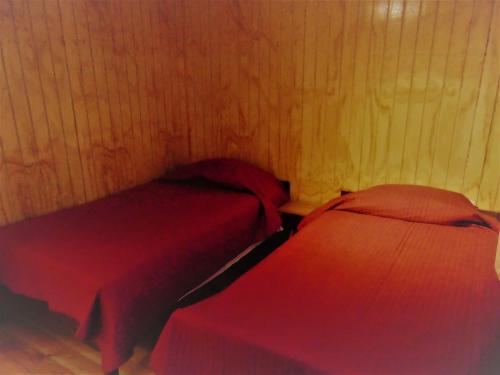 two beds in a room with red sheets at Cafe & Hostal Acurruka in Curacautín