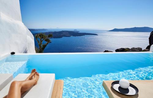 a woman sitting on a bench next to a swimming pool at Villa Etheras in Firostefani