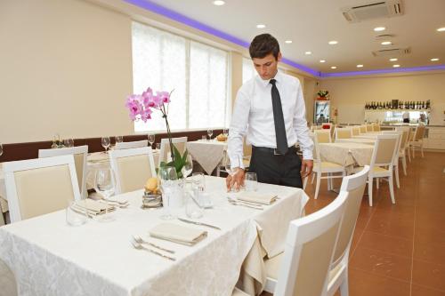 a man in a tie is setting a table in a restaurant at Hotel Albatros 3 Stelle Superior in Lido di Jesolo