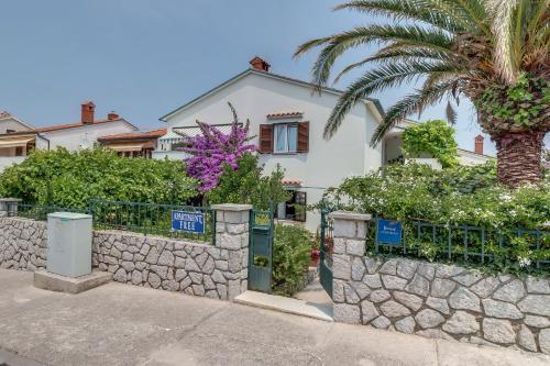 a house with a stone fence and a palm tree at Apartment Marisa in Mali Lošinj