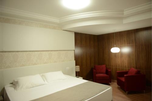 a bedroom with a white bed and a red chair at Hotel Vilhar in Ivaiporã