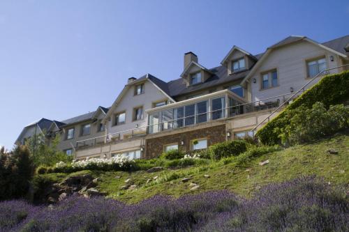 a large house on top of a hill with purple flowers at Amaike Hotel Golf & Spa in Tandil
