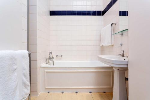 La salle de bains blanche est pourvue d'une baignoire et d'un lavabo. dans l'établissement Veeve - Queen's Gardens Flat, à Londres