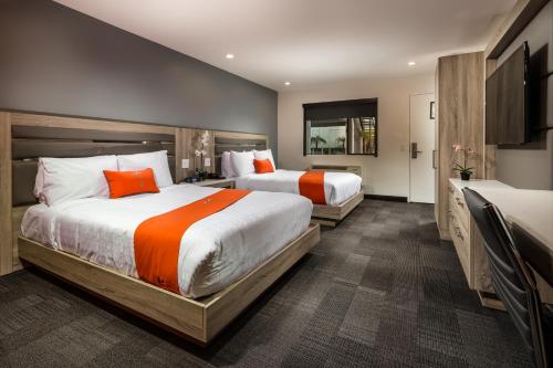 two beds in a hotel room with orange at Canoga Hotel at Warner Center in Canoga Park