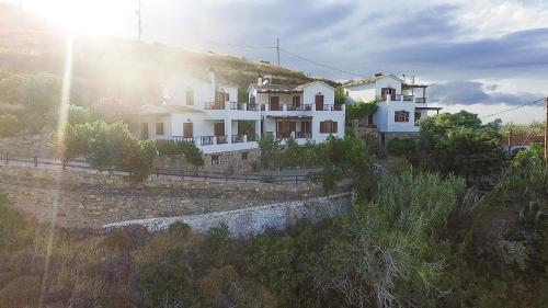 a large white house on a hill with the sun at Ikaria Utopia - Cusco Studios in Évdhilos